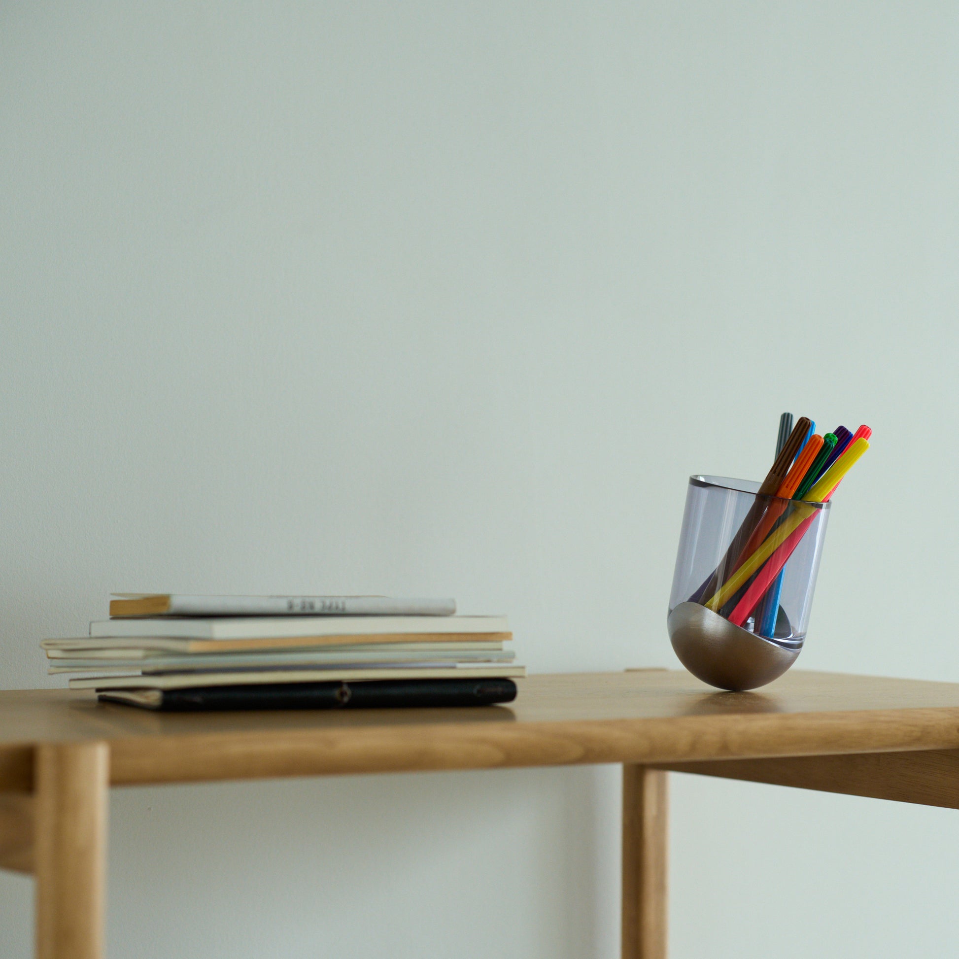 SESEKI/SE-SG-C-08(色:シルバー/グロス/濃い青)/透明な青色のSESEKIにペンを入れ、テーブルの上に置いて小物入れとして使用しているシーン画像