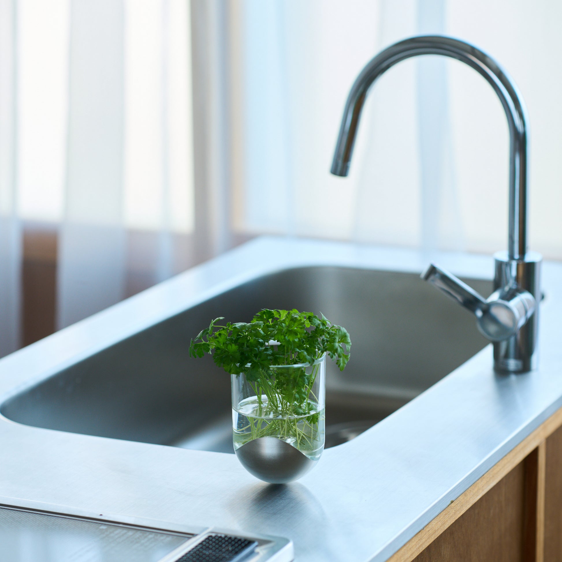 鋳鉄部分は銀色で樹脂部分は無色透明なSESEKIに植物を植えて、キッチンのシンクの上に置き、花瓶として使用しているシーン画像/SESEKI/SE-SG-P-01(色:シルバー/グロス/無色)