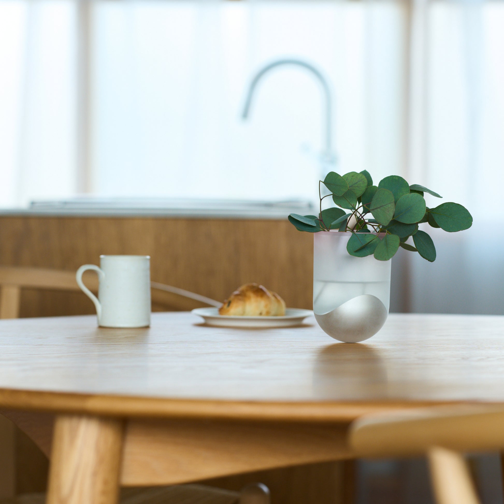 鋳鉄部分がシルバー色で樹脂は半透明(艶消し)なSESEKIに植物を入れ、テーブルの上に置いて花瓶として使用しているシーン画像/SESEKI/SE-SM-P-02(色:シルバー/マット/無色)